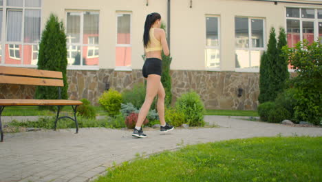 A-woman-makes-lunges-on-a-sidewalk-path-in-a-park-in-an-urban-environment.-Slow-motion-shooting-of-a-woman-in-sportswear-steps-with-a-lunge